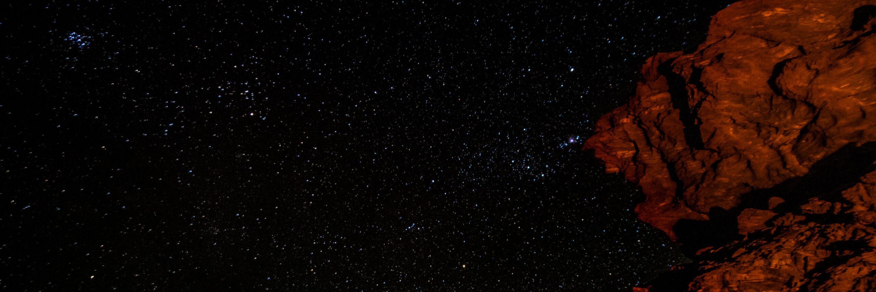 Sternenhimmel mit von Lagerfeuer beleuchtetem Fels im Vordergrund