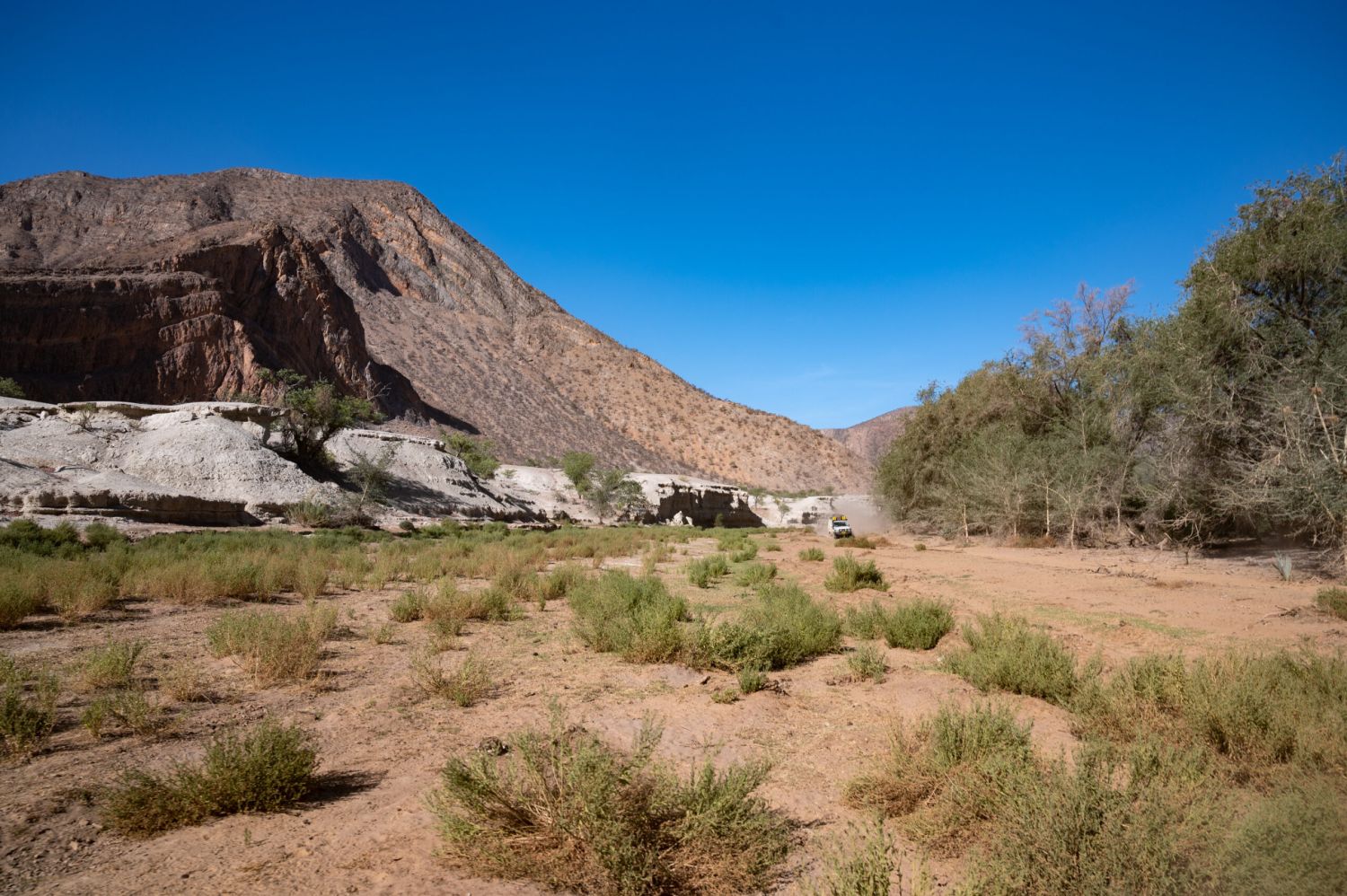 Offroadfahrzeug fährt weit hinten im Bild über Wüstenlandschaft auf Kamera zu
